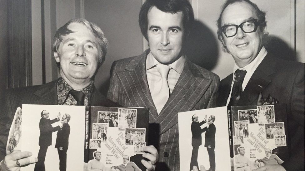 Ernie Wise, Colin Webb and Eric Morecambe holding copies of a book they were all involved in creating