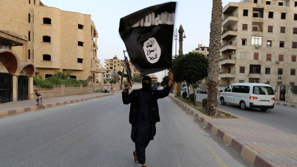 A lone armed and masked Islamic State militant waving an ISIS / ISIL flag, on a deserted street in Raqqa, June 2014