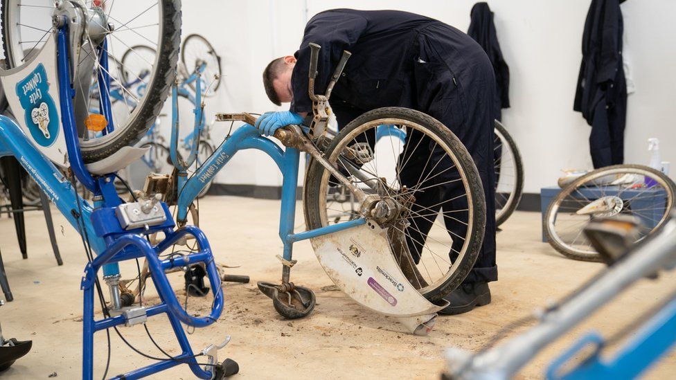 Man works on a bike which is upside down. Other bikes are visible.