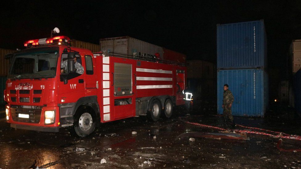 Fire engine and fire fighter beside shipping containers set on fire by suspected Israeli strike on Latakia port, Syria (7 December 2021)