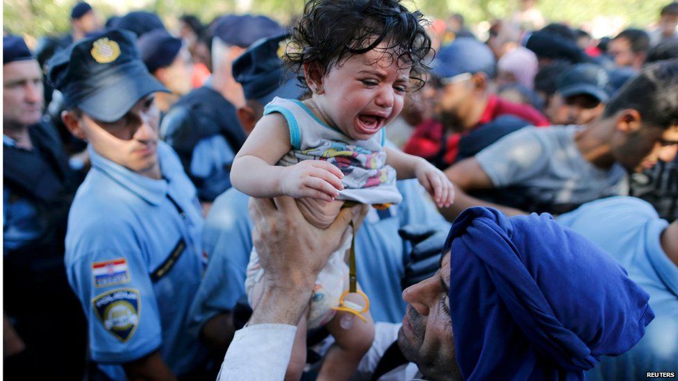 A migrant lifts a crying baby as he waits to board a bus in Tovarnik, Croatia, September 17, 2015