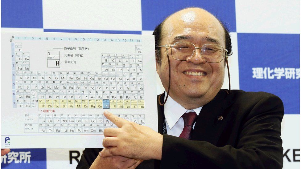 Kosuke Morita of Riken Nishina Center for Accelerator-Based Science points at periodic table of the elements.
