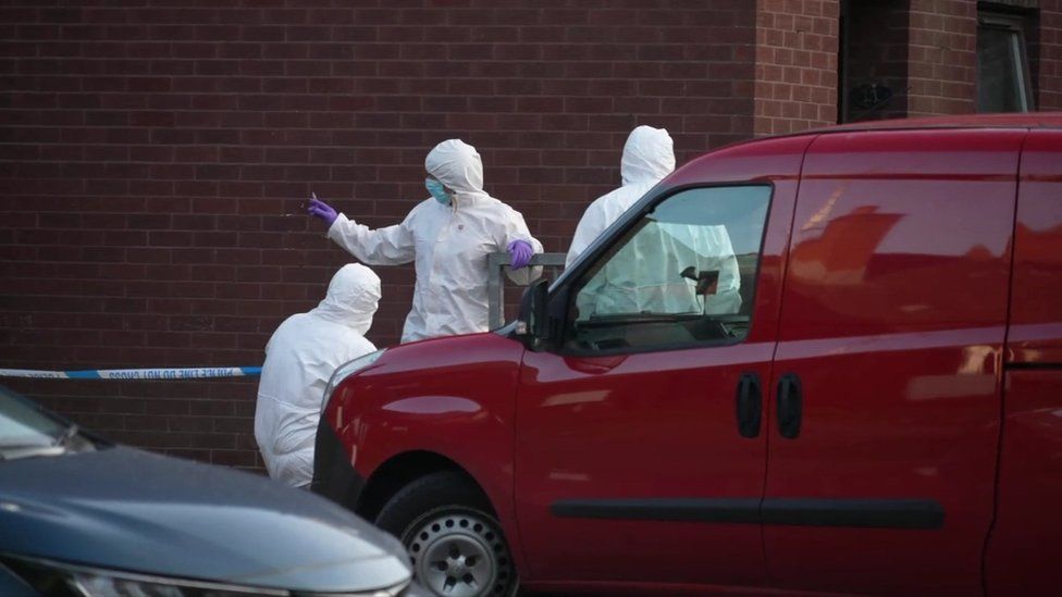 Forensics officers in white suits stand next to a red van