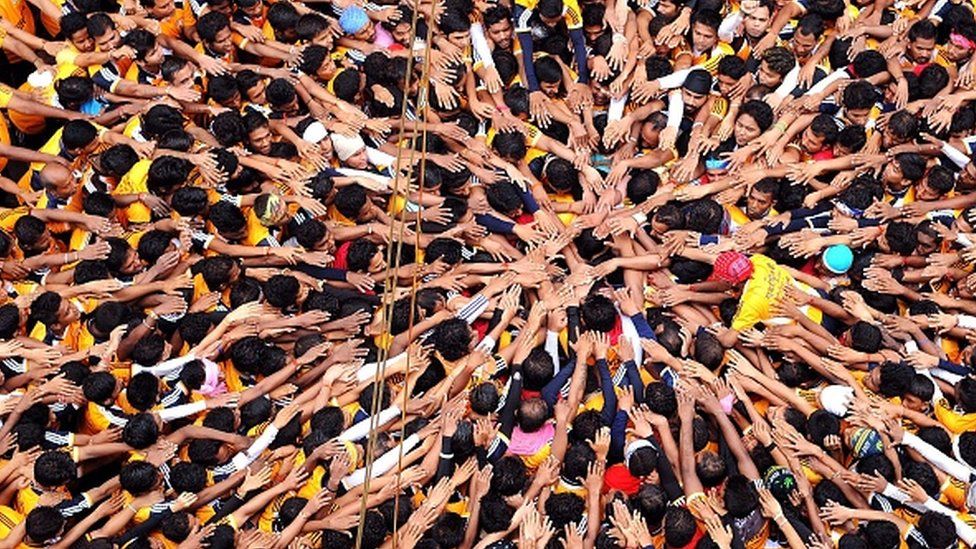 Индийские преданные-индуисты жестикулируют перед попыткой сформировать человеческую пирамиду, пытаясь достать и разбить дахи-ханди (творожный горшок), подвешенный в воздухе во время празднования фестиваля Джанмаштами, который знаменует рождение индуистского бога Господа Кришны, в Мумбаи 24 декабря. 18 августа 2014 года.