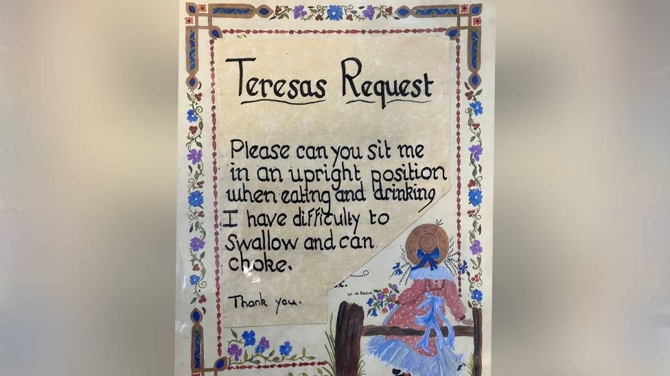 Family sign put above Mrs Pokoyski's bed which reads: Teresas Request. Please can you sit me in an upright position when feeding and drinking. I have difficulty to swallow and can choke. Thank you.