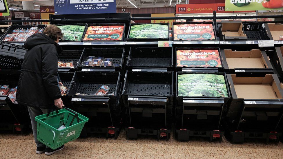 Woman in front of depleted vegetable shelves