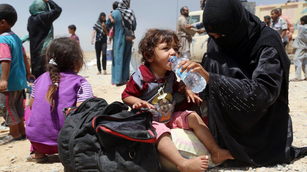 A displaced Iraqi woman helps a child drink water at a camp outside Irbil (15 July 2016)