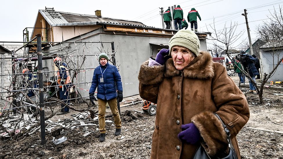 A woman in front of damaged buildings