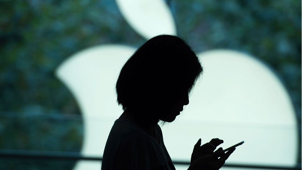 A young woman holding an iPhone in front of the Apple logo