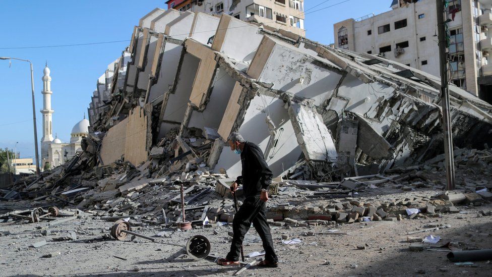 A Palestinian man walks past the remains of a tower block in Gaza City that was destroyed in an Israeli air strike (12 May 2021)