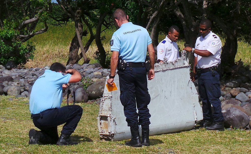 French gendarmes and police inspect a large piece of plane debris which was found on the beach in Saint-Andre, on the French Indian Ocean island of La Reunion, 29 July 2015.