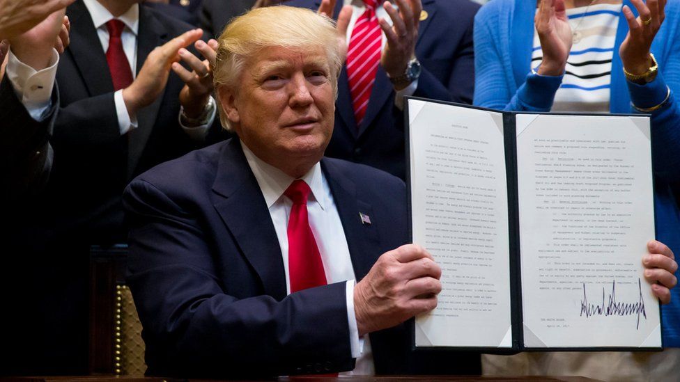 Donald Trump holds up an executive order while people behind him clap