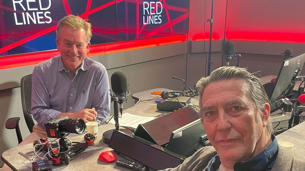 Ciarán Hinds sits in a radio studio with BBC presenter Mark Carruthers