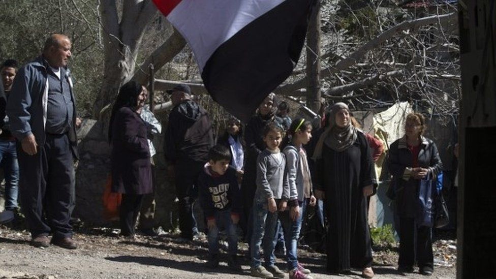 Syrians wait for the distribution of humanitarian aid near a Russian military truck in the village of Ghunaymiyah