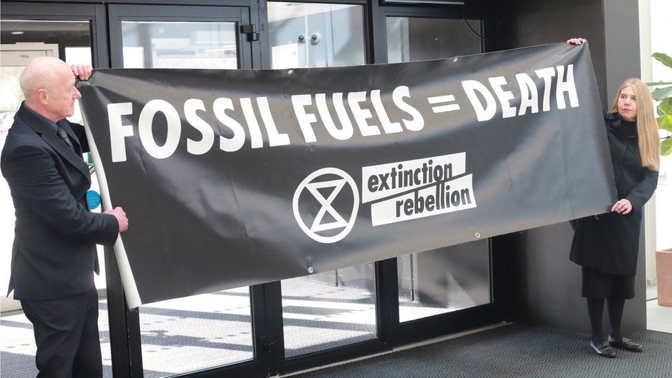 Extinction Rebellion protestors at Barclaycard headquarters in Northampton with a sign saying "Fossil Fuels = Death"