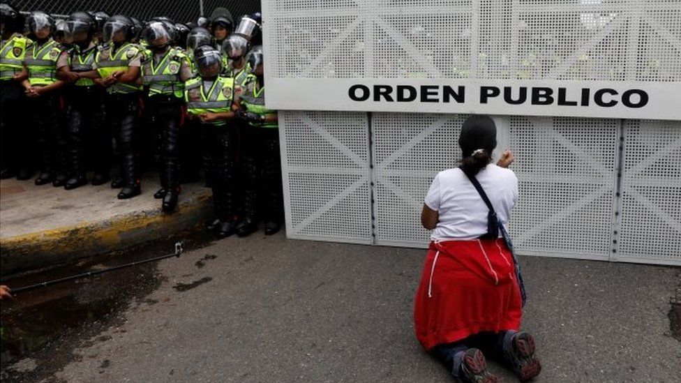 A woman kneels down front of riot police during Caracas protest 22 April 2017