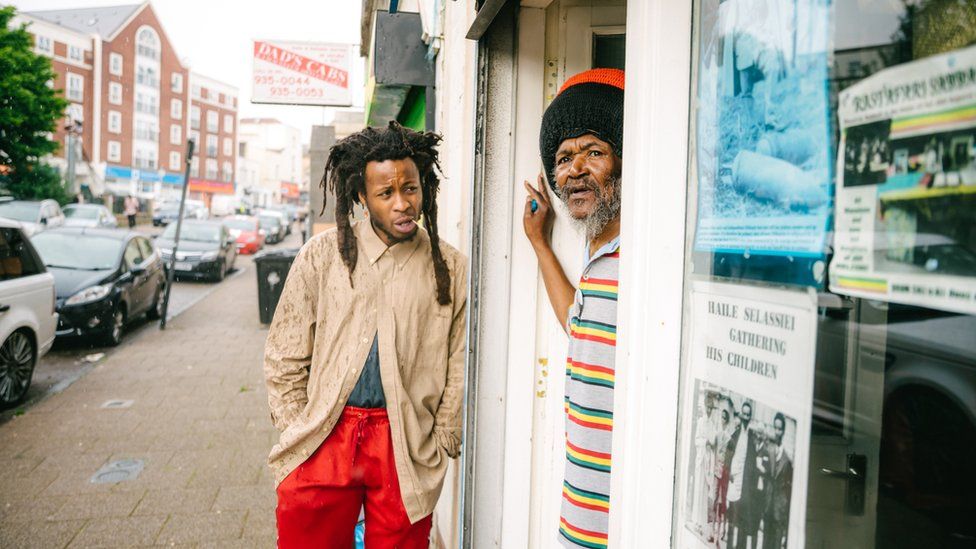 Mr Ogunmefun-Brooker leaning on a wall and Ras Bandele Selassie looking out of the door