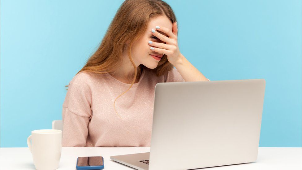 In this stock photo, a woman holds her hand to her face in frustration in front of a laptop computer, illustrating the realisation of a mistake