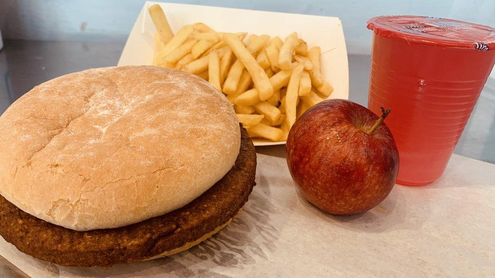 A burger, chips, apple and soft drink meal on a table
