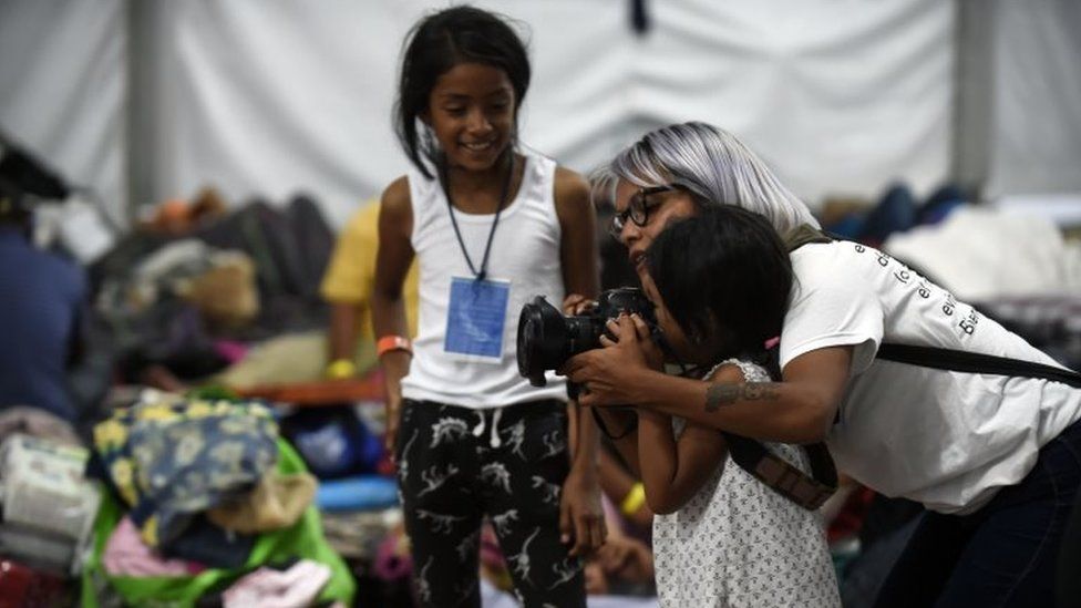 A photographer shows a young migrant girl how to use her camera