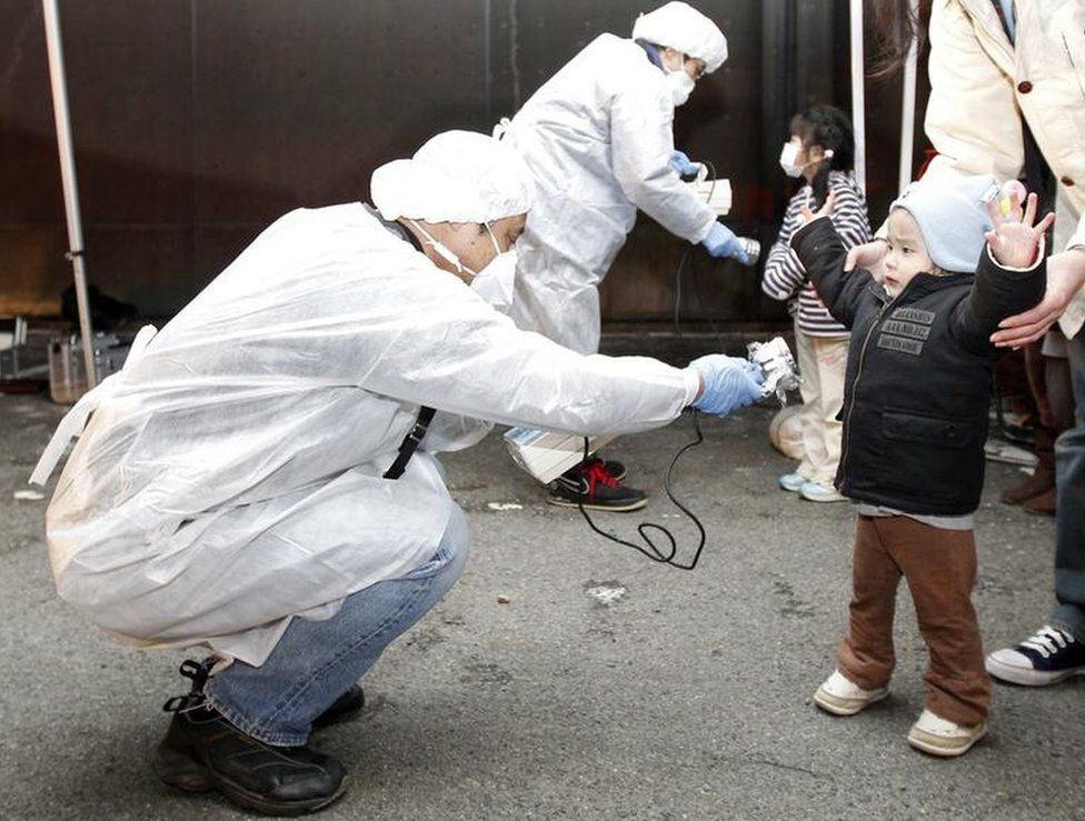 Officials in protective gear check for signs of radiation on children from the evacuation area near the Fukushima plant in March, 2011