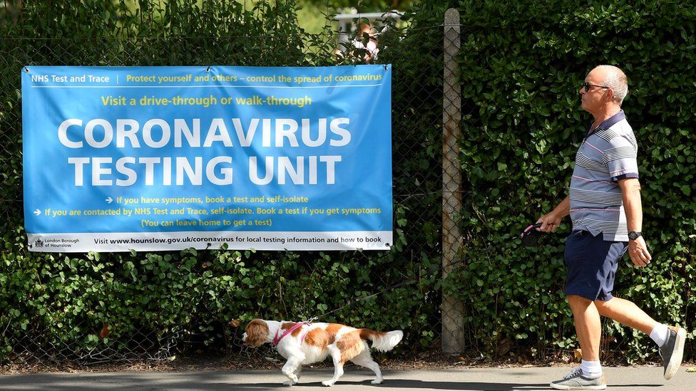 A man walks his dog past a poster promoting the coronavirus disease (COVID-19) testing at local mobile test centres, in Hounslow