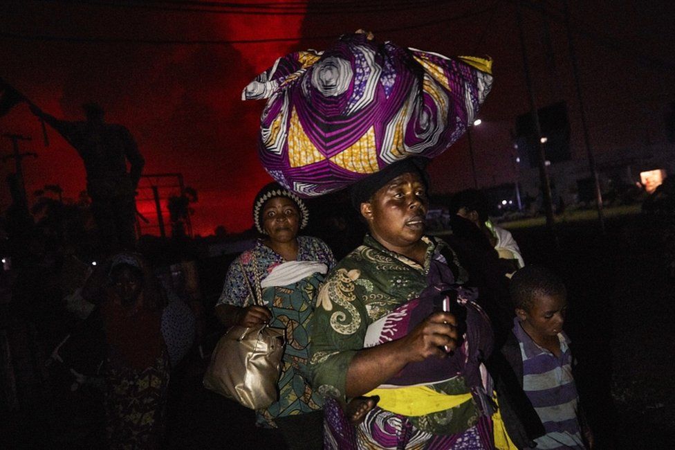 A Congolese woman, carrying possessions on her head, flees from Mount Nyiragongo volcano as it erupts over Goma, Democratic Republic of the Congo, on 22 May 2021