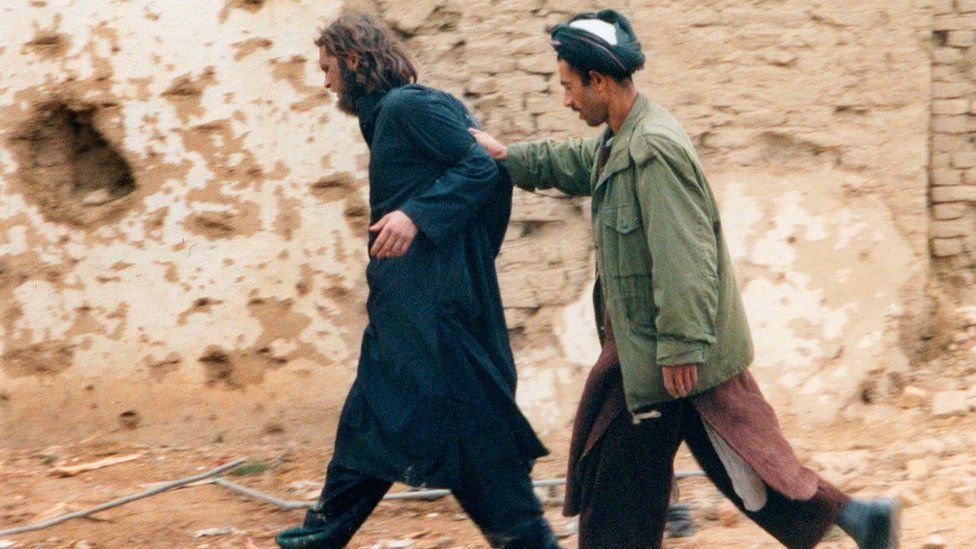John Walker Lindh (left) is led away by a Northern Alliance soldier after he was captured among al Qaeda and Taliban prisoners in 2001