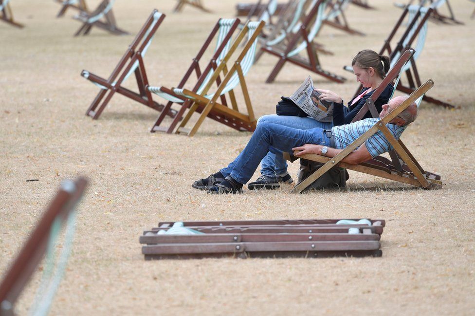 A couple relax on deckchairs on parched grass in Hyde Park in London.