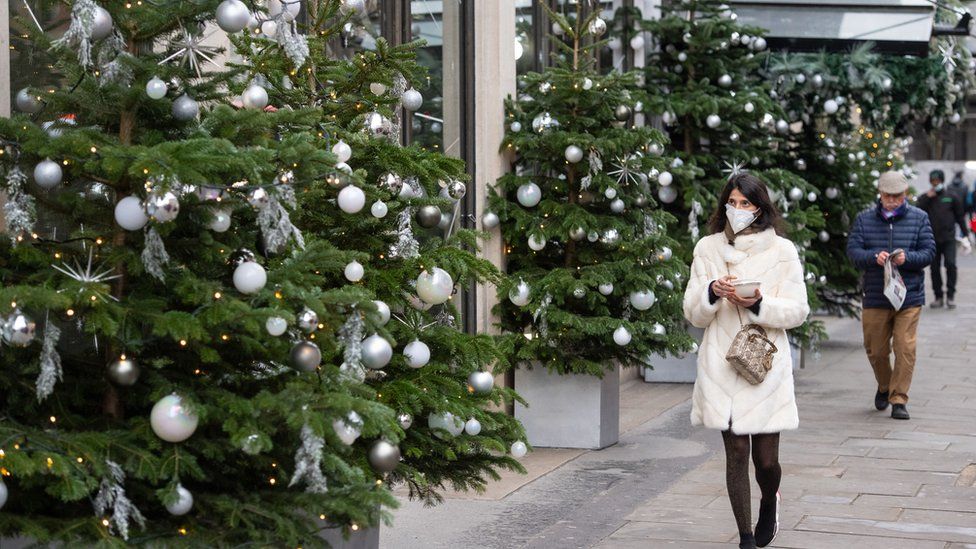A woman wearing a face mask walks passes a display of Christmas trees outside a shop in central London,