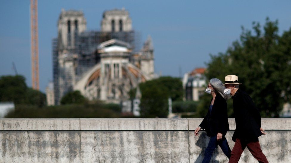 Two people in face masks walk past Notre-Dame in Paris