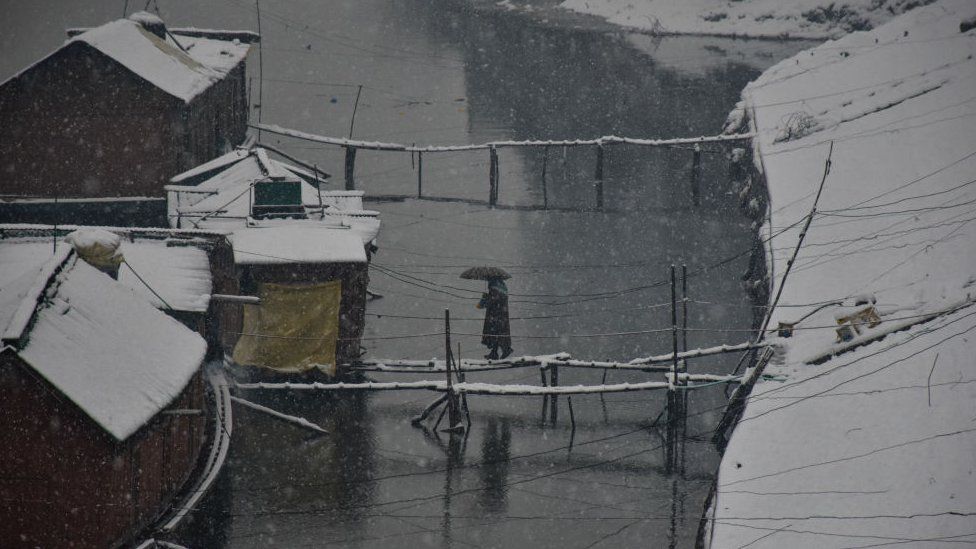 A Женщина идет к своему плавучему дому во время снегопада в Шринагаре. Кашмирская долина была отрезана от внешнего мира, все рейсы в аэропорт Сринагара и обратно были отменены, а национальная автомагистраль была перекрыта из-за сильного снегопада в понедельник утром.