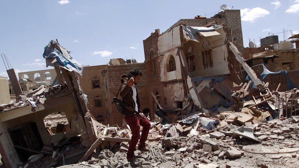 An armed Yemeni man on the ruins of buildings destroyed in an air strike by the Saudi-led coalition in Sanaa