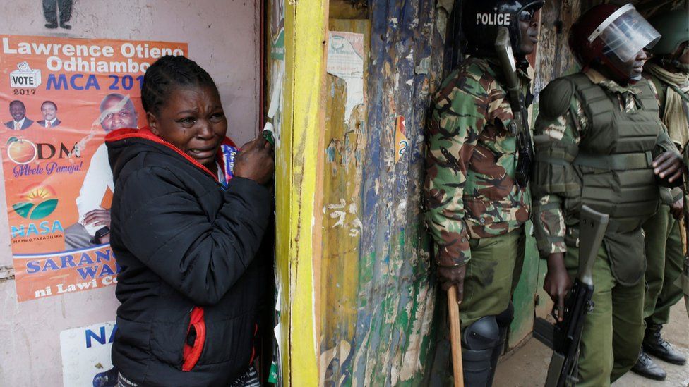 Woman shelters behind police during clashes in Kibera slum