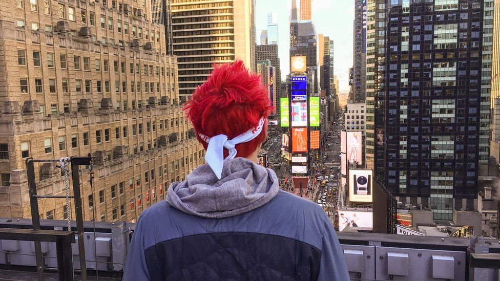 Ninja looks out over a skyscape of New York. His two trademarks are most visible - fluorescent, coloured hair and a bandana.