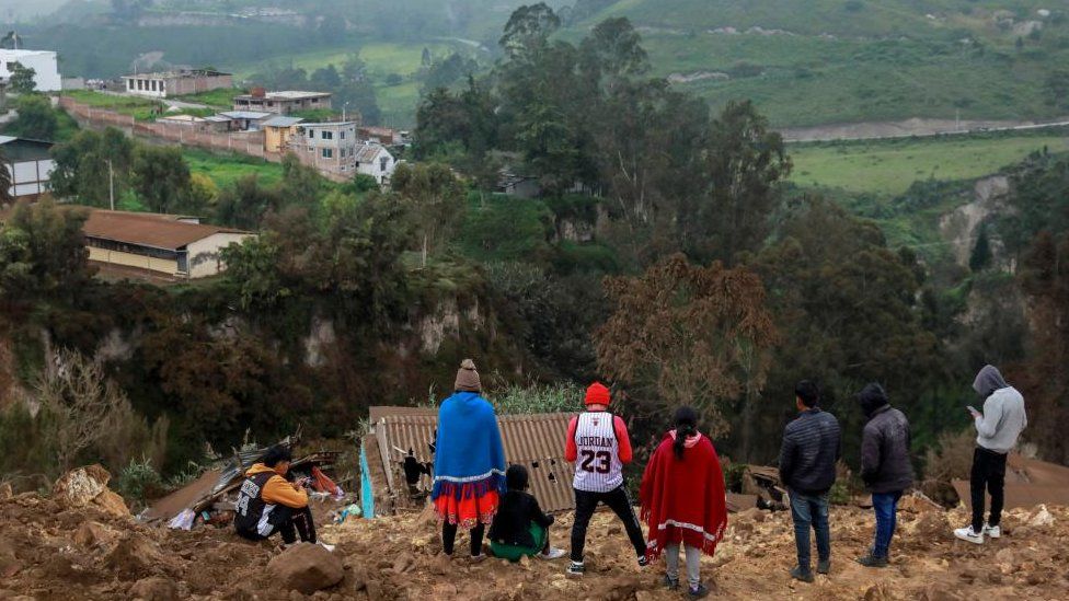 People stand near a damaged house, following a landslide in Alausi, Ecuador March 27, 2023.