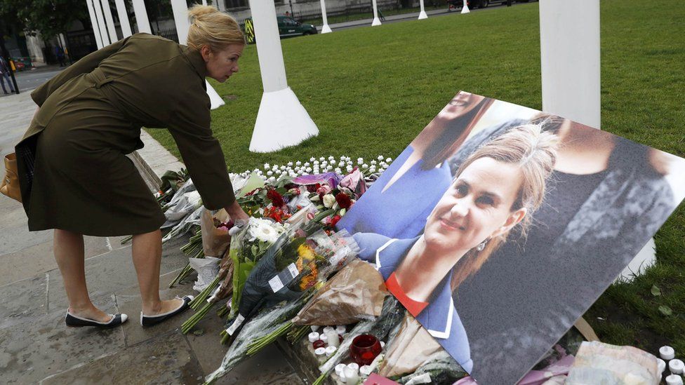 Woman laying flowers in front of a photograph of Jo Cox
