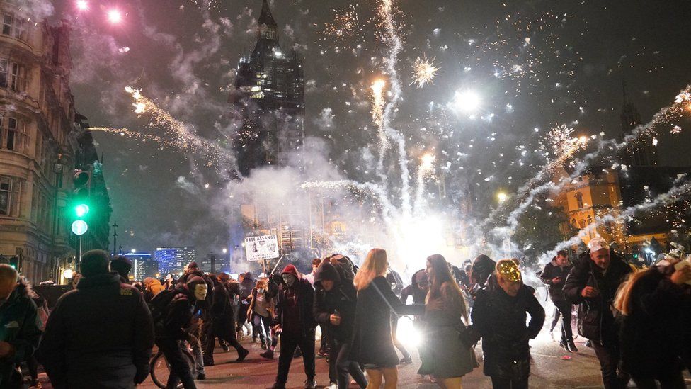 Firework being set off close to a group of demonstrators with the Palace of Westminster in the background