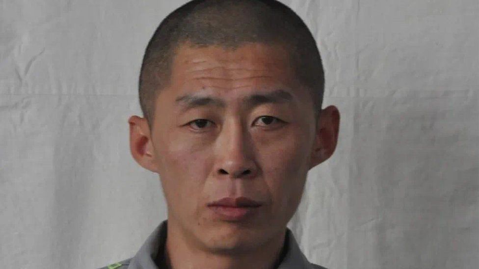 North Korean prisoner Zhu Xianjian stands against grey backdrop