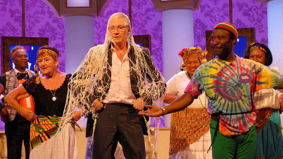 Paul O'Grady, covered in fake cobwebs and with performers around him