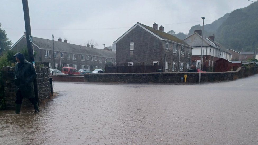 Man in a raincoat walks alongside a flooded road in Port Talbot
