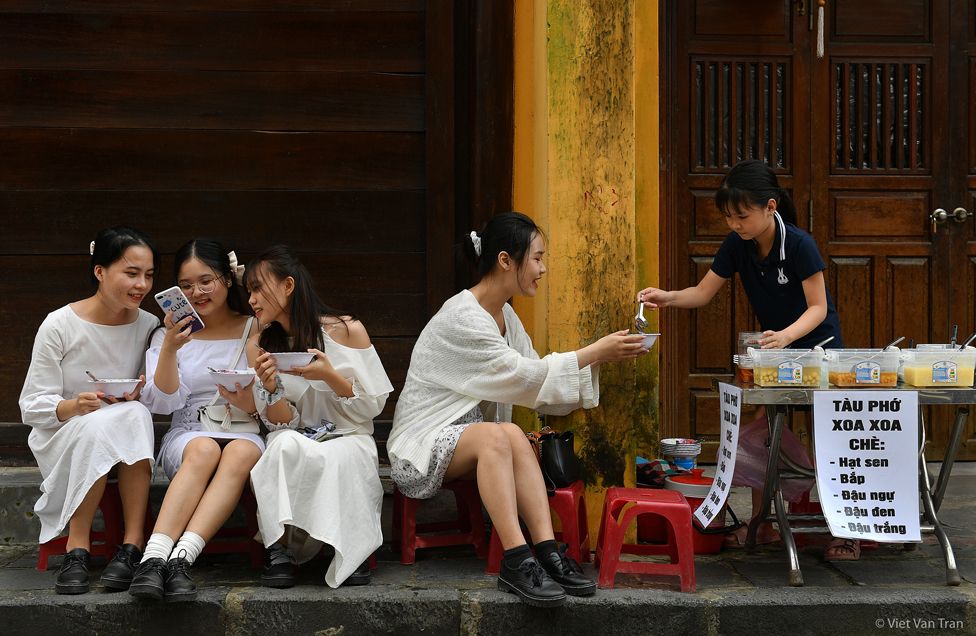 A woman serves food to a group of young women, sitting outdoors