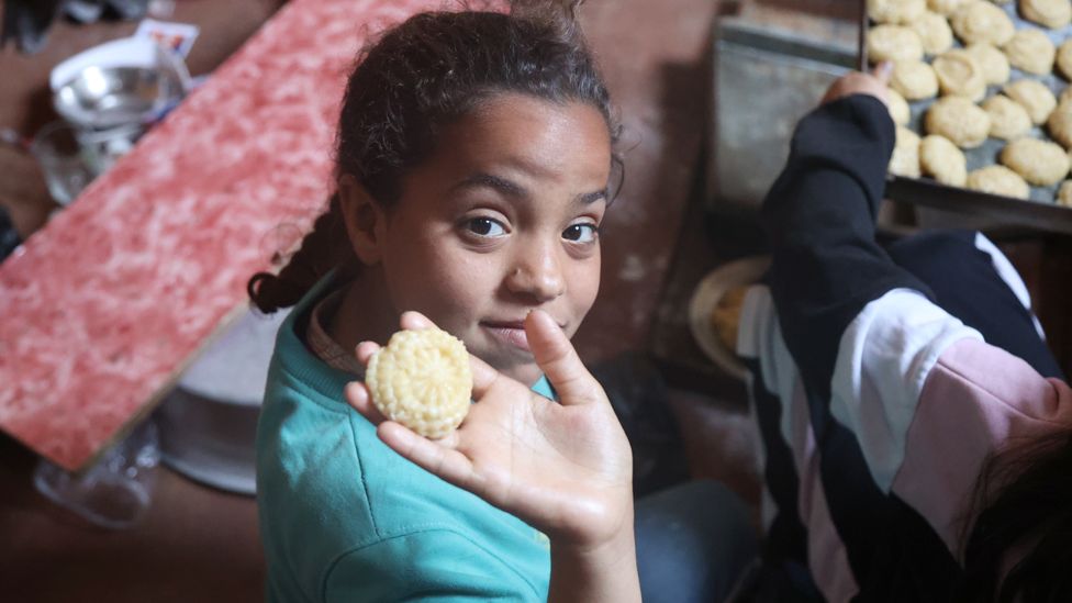 A girl holds up an uncooked kahk biscuit in Cairo, Egypt - Sunday 7 April 2024