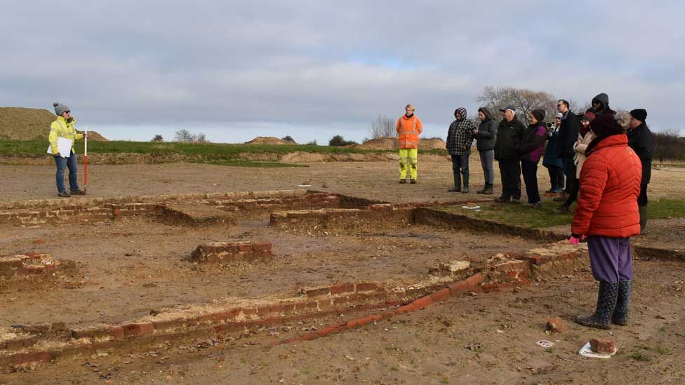 Archaeologists show a tour group the most well preserved building on site