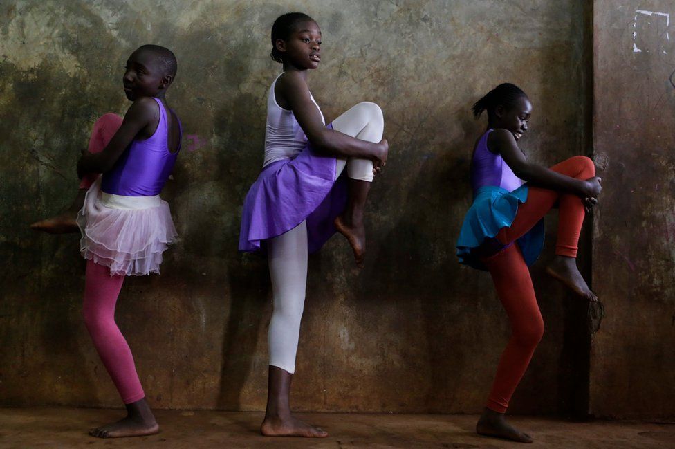 Young ballerinas dressed in leotards and tutus stretch their legs before a lesson