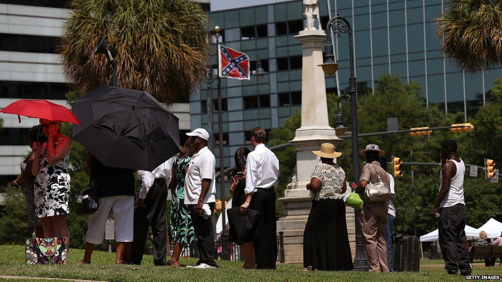 People queuing as a confederate flag remains above them