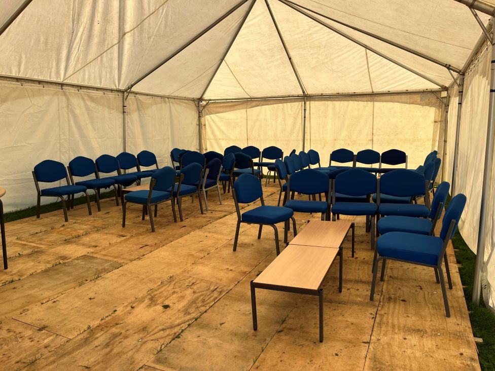 The inside of the marquee shows a temporary floor and blue seats and low tables arranged inside.