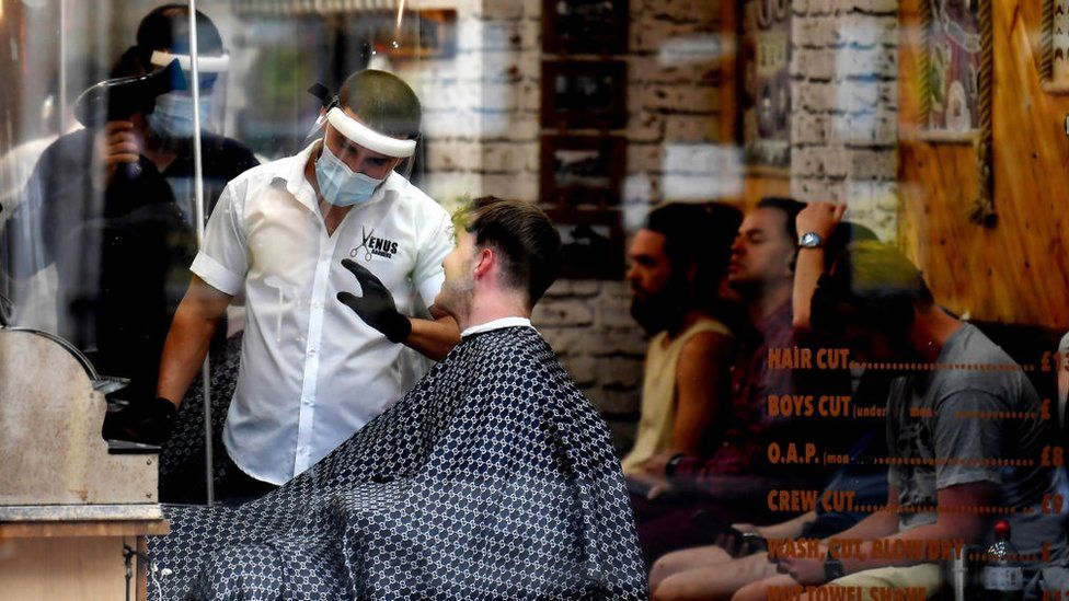 Barbers in masks serve customers as many others wait their turn in Clapham