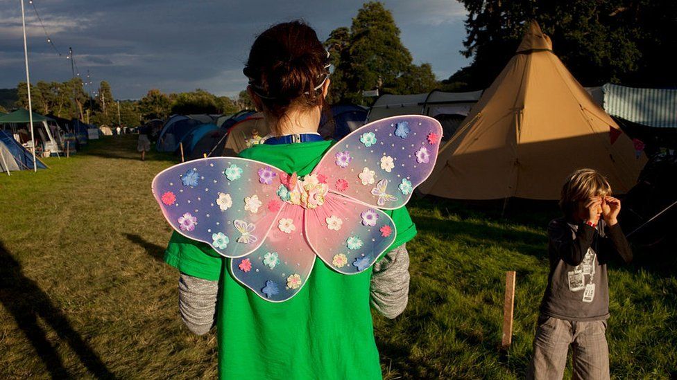 A person with angel wings walks through the family section of the campsite at the Green Man Festival