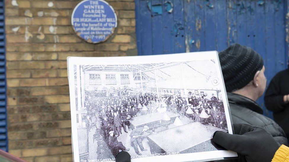 A person standing in front of the Winter Gardens in Middlesbrough, looking at a historic photograph of the building